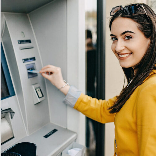 Ein Symbolbild einer Frau, die an einem Bankautomaten ihre Bankkarte verwendet.