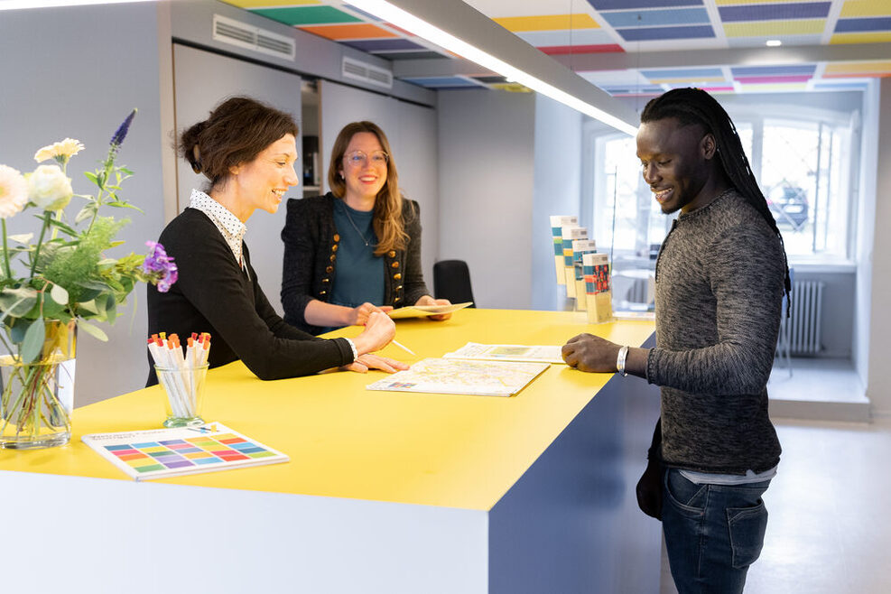 Eine Beratungssituaion im Welcome Center Stuttgart. Zu sehen sind zwei Mitarbeiterinnen und ein Mann, alle drei Stehen an einem Tisch.