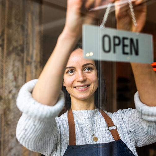 Eine junge Frau steht in der Eingangstür eines Geschäfts und lächelt in die Kamera.