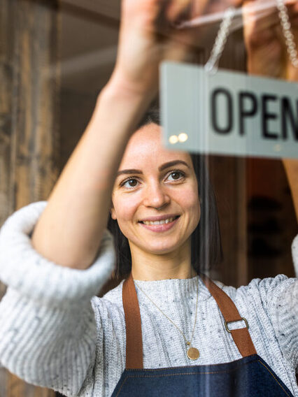 Eine junge Frau steht in der Eingangstür eines Geschäfts und lächelt in die Kamera.