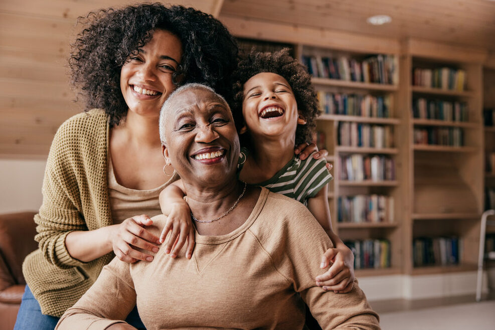 Drei Generationen von Frauen sitzen in familiärer Nähe zueinander und lächeln.