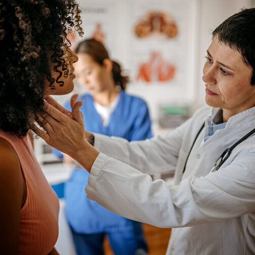 Eine Ärztin untersucht den Hals einer Patientin.